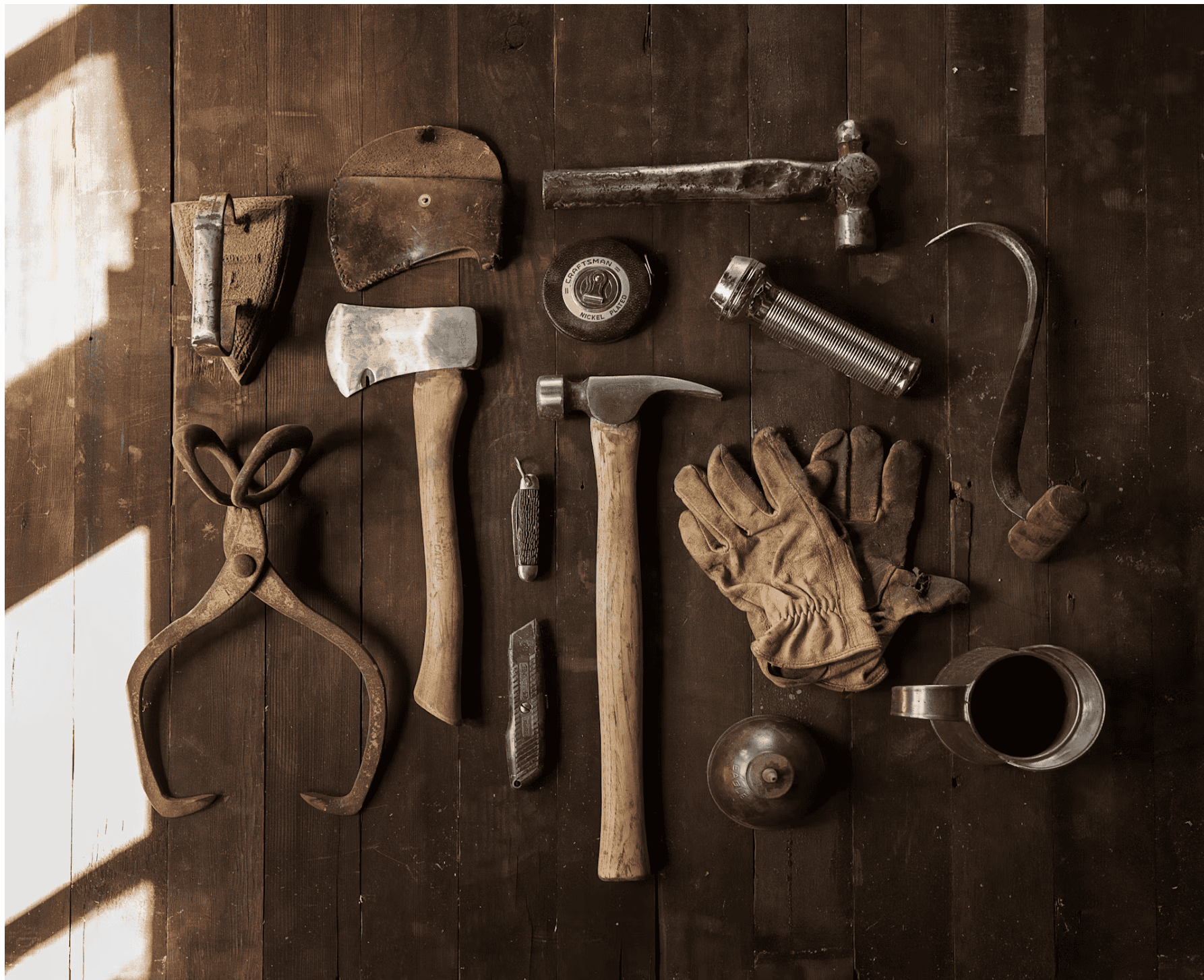 Hand tools laid out on worn wood with empty slots in the row where tools are missing — the cool weight of metal, the grain of an old workbench.